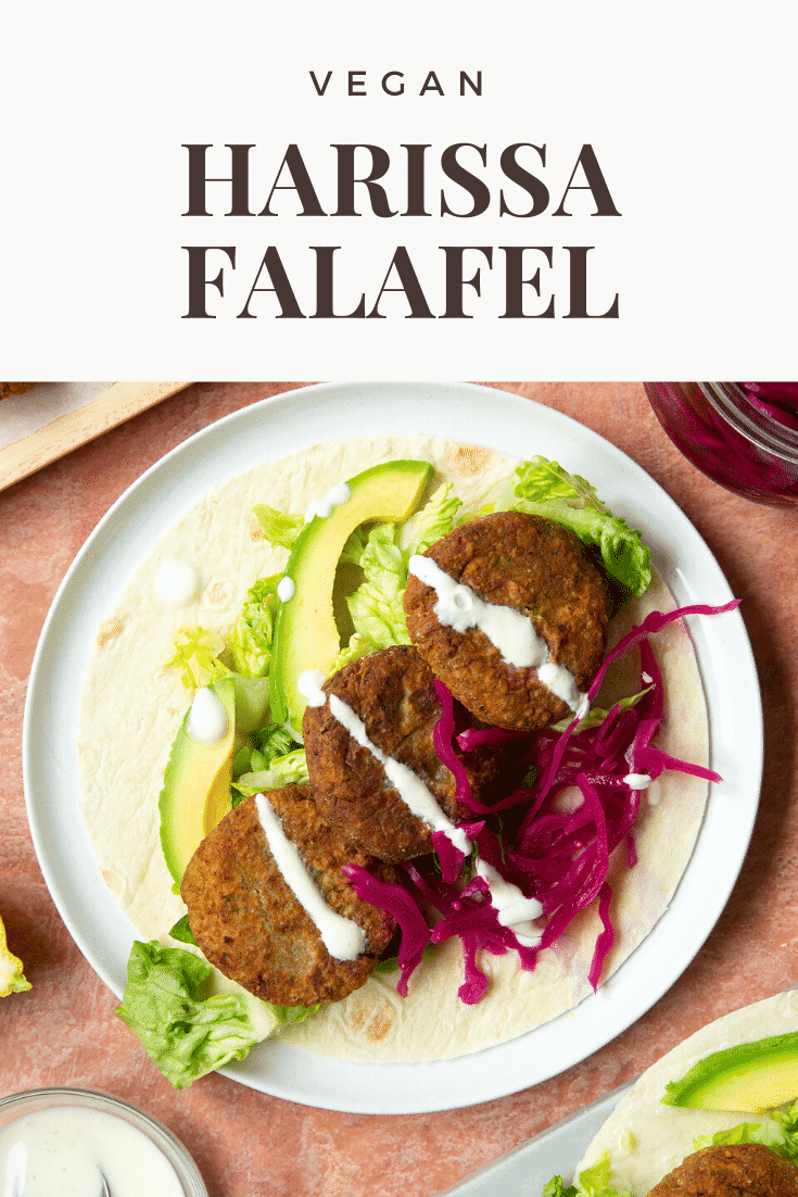 A harissa falafel wrap arranged on a plate with pickled cabbage and salad, drizzled with tahini dressing. The text caption reads, vegan harissa falafel.