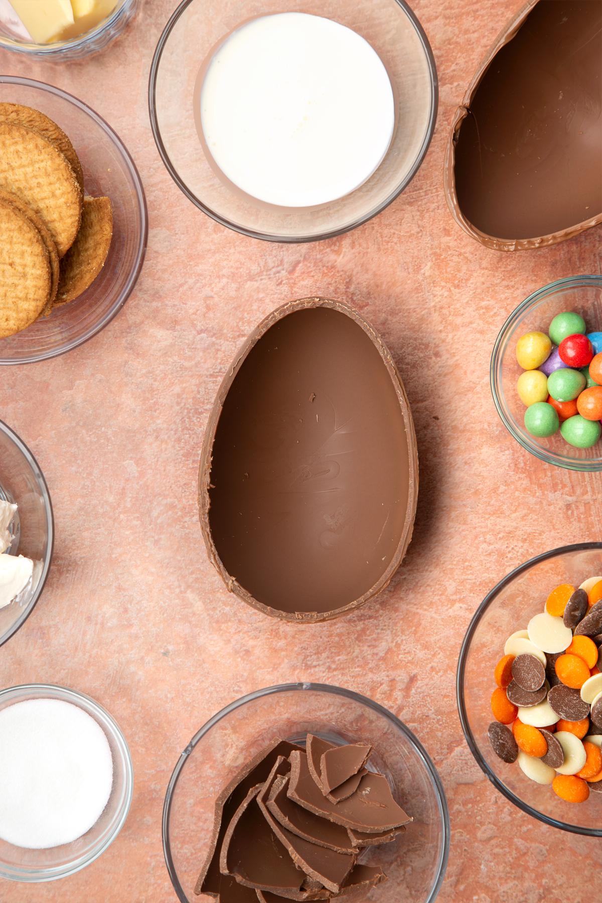 Half a chocolate Easter egg, cut side up. The egg is surrounded by ingredients to make Easter Egg cheesecake.