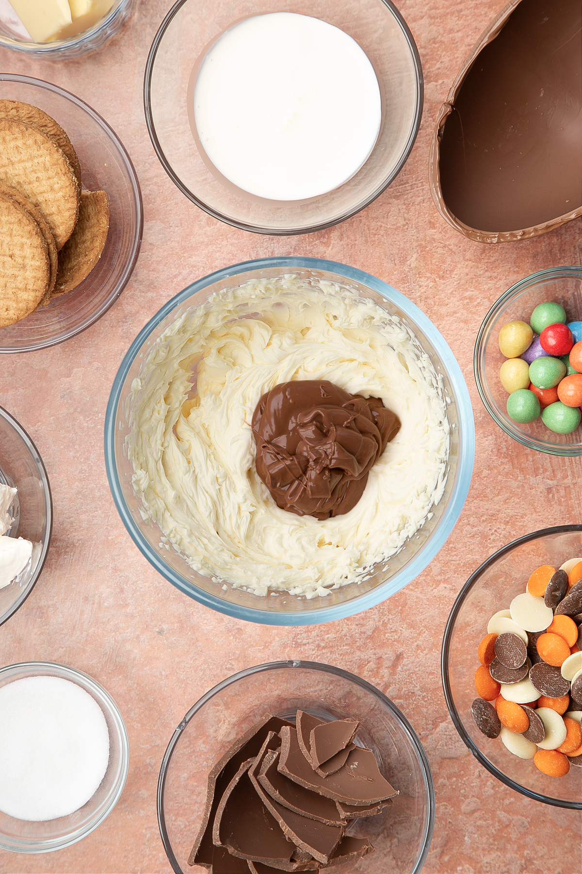 A glass bowl containing cream cheese, double cream and sugar whisked together with melted chocolate. The bowl is surrounded by ingredients to make Easter Egg cheesecake.