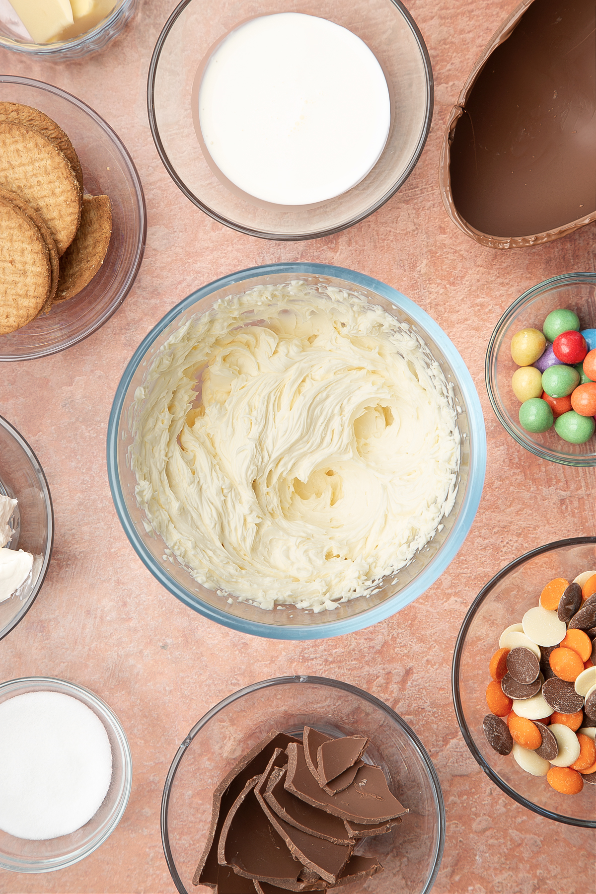 A glass bowl containing cream cheese, double cream and sugar whisked together. The bowl is surrounded by ingredients to make Easter Egg cheesecake.