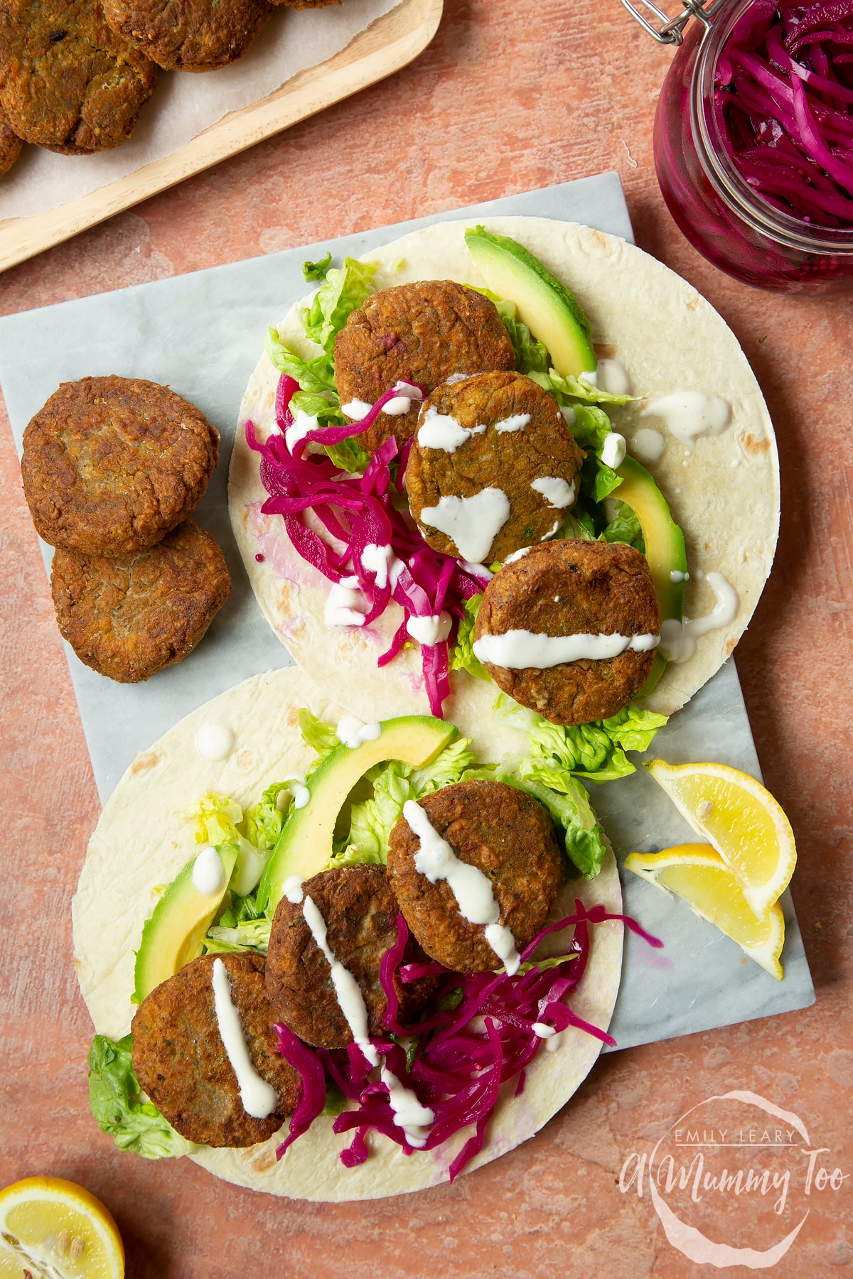 Two harissa falafel wraps arranged on a board with pickled cabbage and salad. Drizzled with tahini dressing.