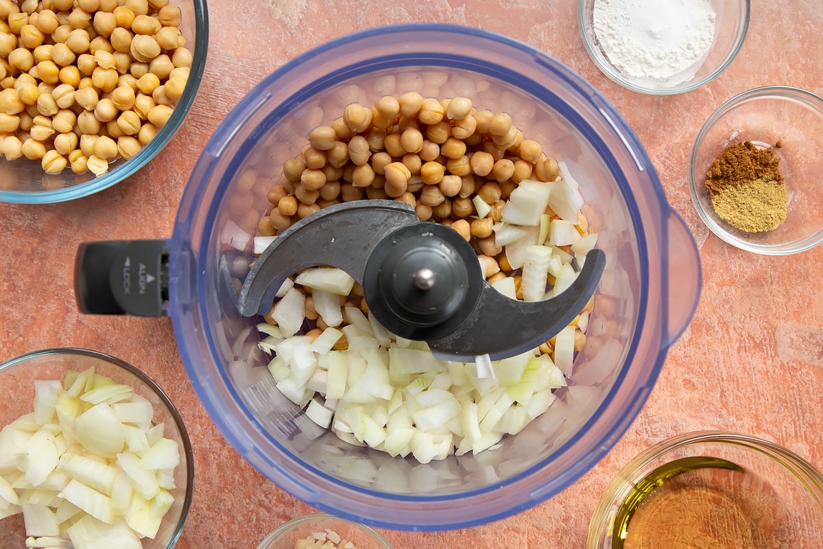 A food processor containing chickpeas and chopped onion for harissa falafel.