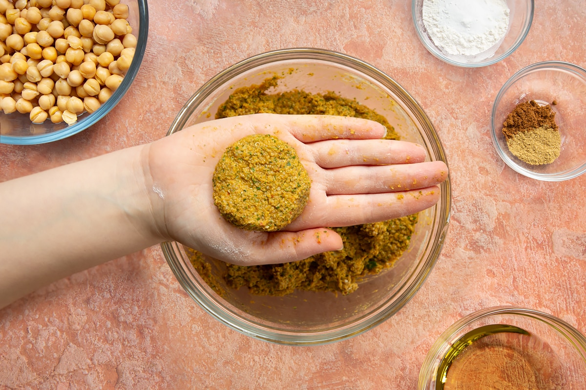 A hand holds a harissa falafel patty over a bowl of harissa falafel mix.