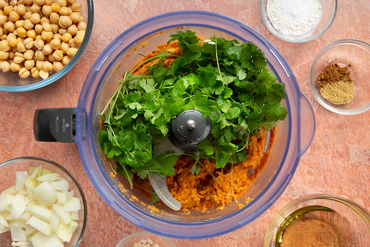 A food processor containing a harissa falafel paste made from chickpeas, spices, garlic, flour, baking powder and chopped onion. Topped with fresh parsley and coriander.