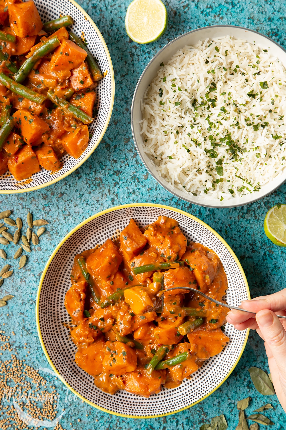 Vegan Sri Lankan curry in two yellow and black bowls, shown from above. Ingredients are scattered around it. A fork lifts some curry from the lower bowl.