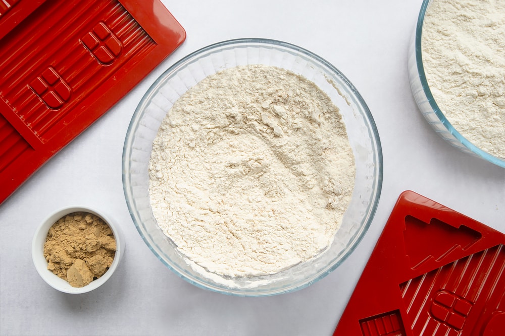 A bowl, surrounded by equipment to make a gingerbread house. In the bowl is flour, mixed with ground ginger and bicarbonate of soda. 