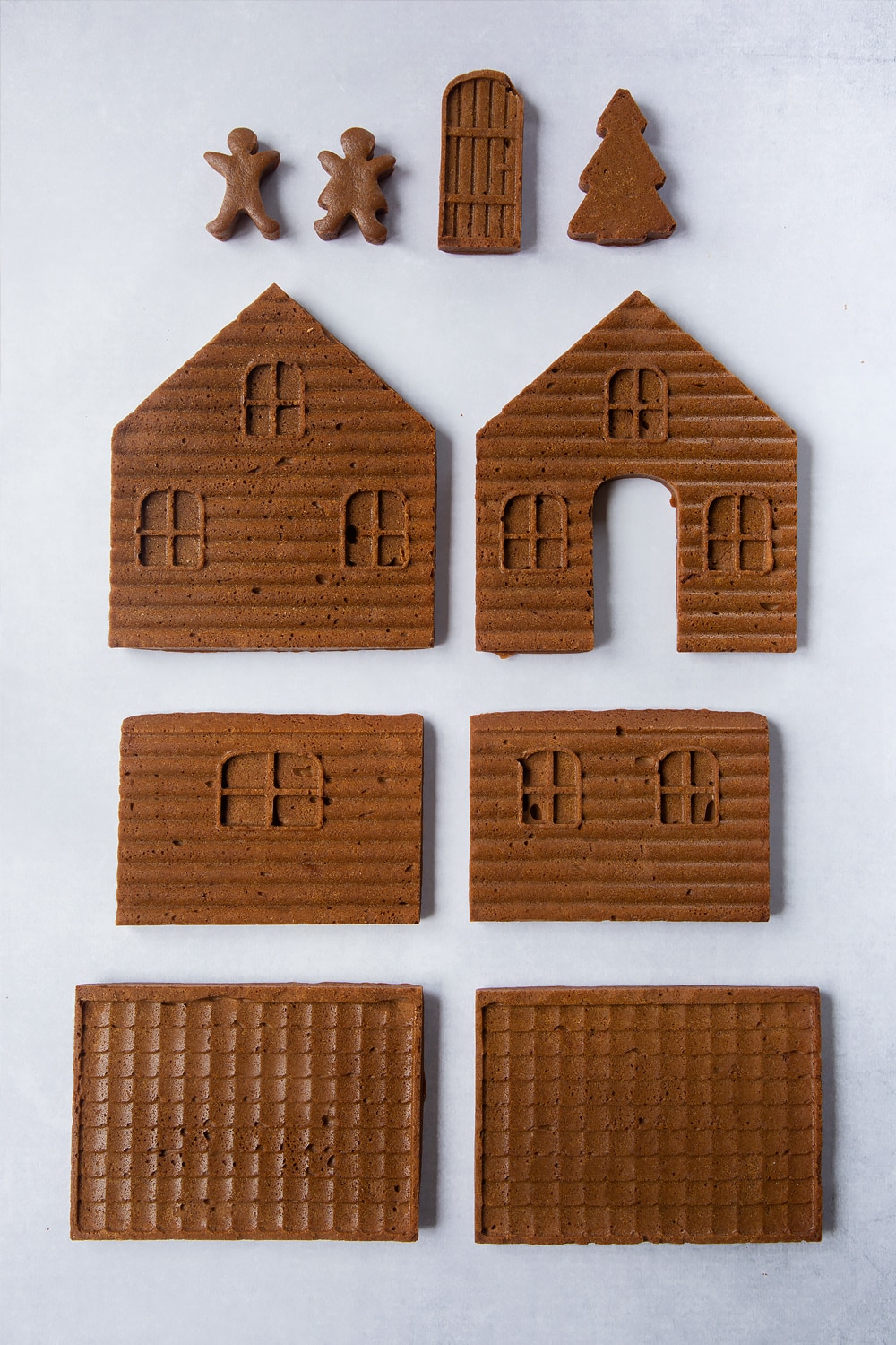 Freshly baked pieces of gingerbread dough, made in a silicone mould so that they form the walls, roof, door, people and Christmas tree to construct into a gingerbread house.