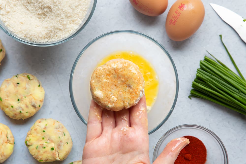 Dipping the fishcake in a beaten egg mixture. 