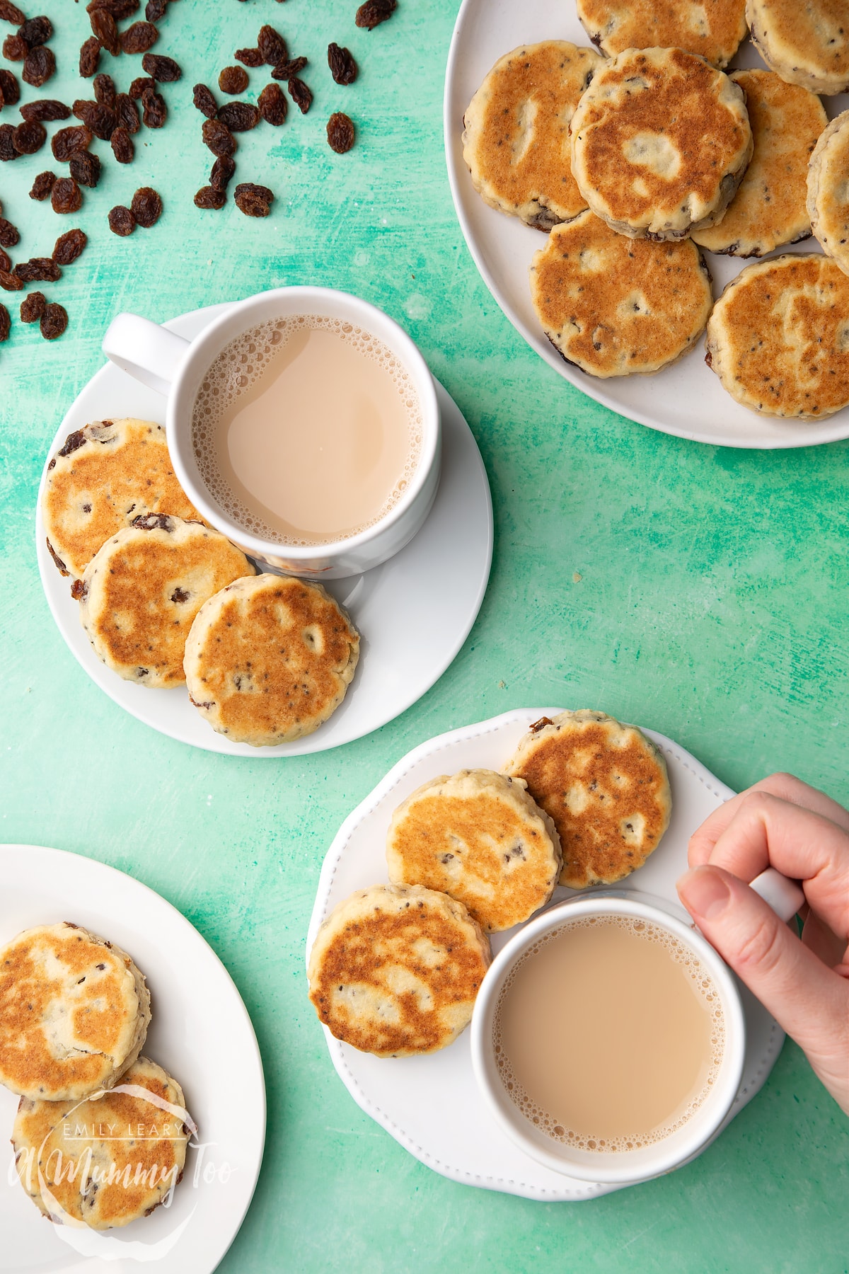 Vegan Welsh cakes arranged on a white plates with cups of tea. A hand reaches in to take a cup.