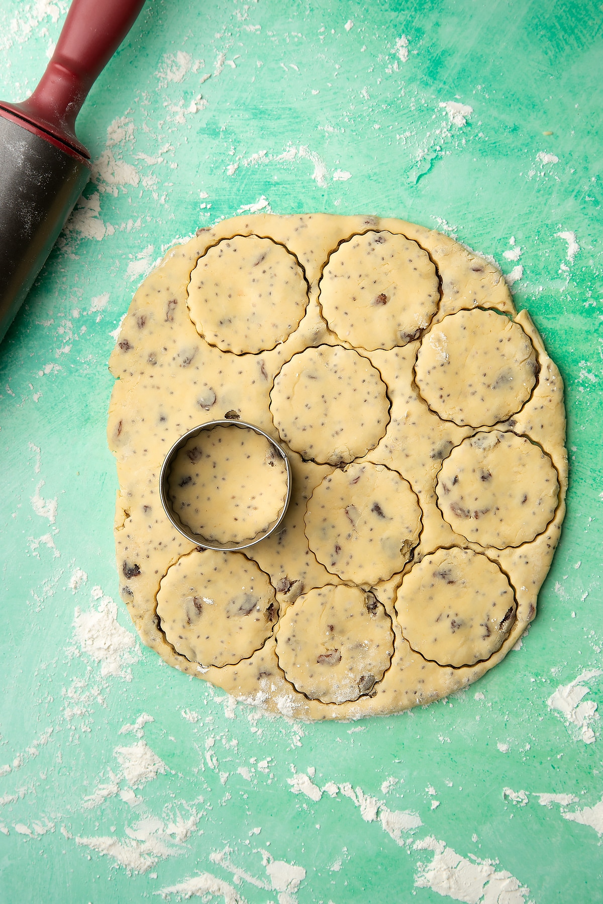 Vegan Welsh cakes dough rolled out on a floured surface. A cookie cutter is shown and has cut out several discs.