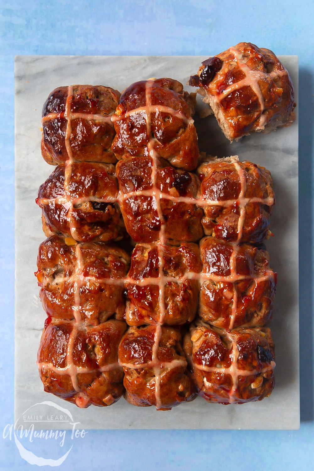 12 vegan hot cross buns on a marble board. One is lifted away from the others.