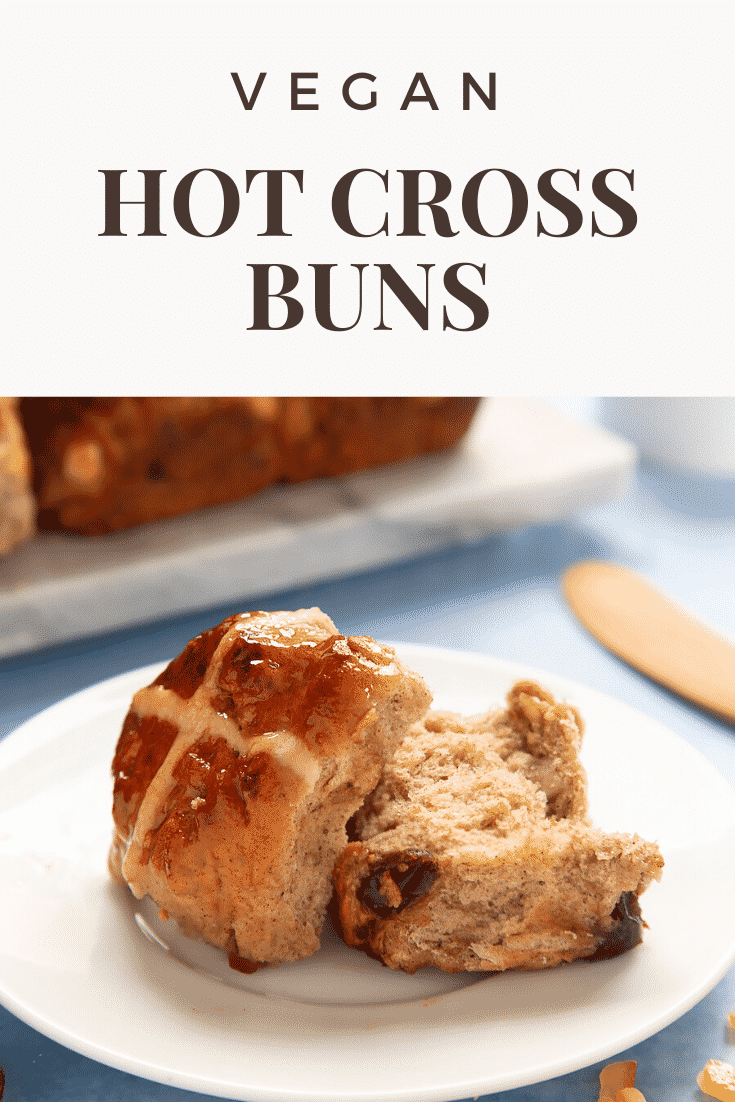 A freshly baked vegan hot cross bun on a white plate, cut open. Caption reads: vegan hot cross buns