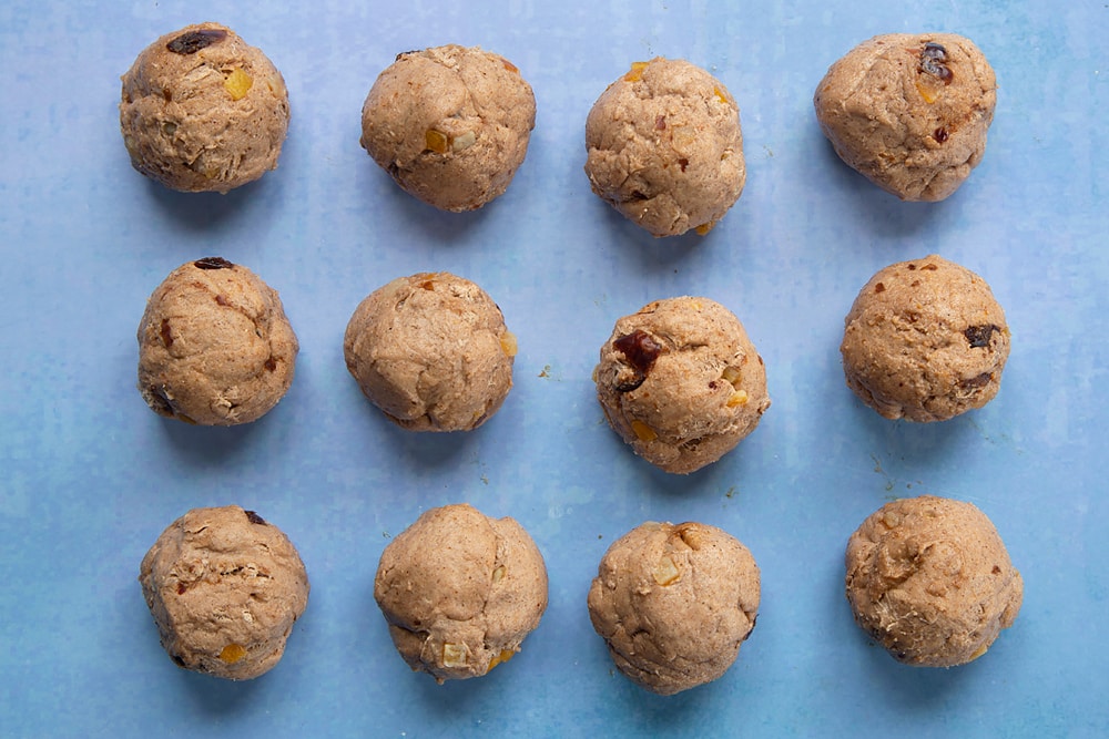 Vegan hot cross buns dough with mixed peel and chopped dates, divided into 12 balls.