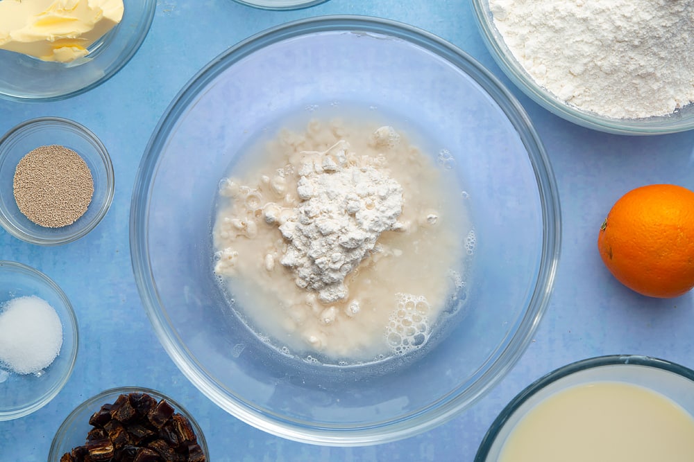 A bowl containing flour and water. The bowl is surrounded by the ingredients to make vegan hot cross buns.