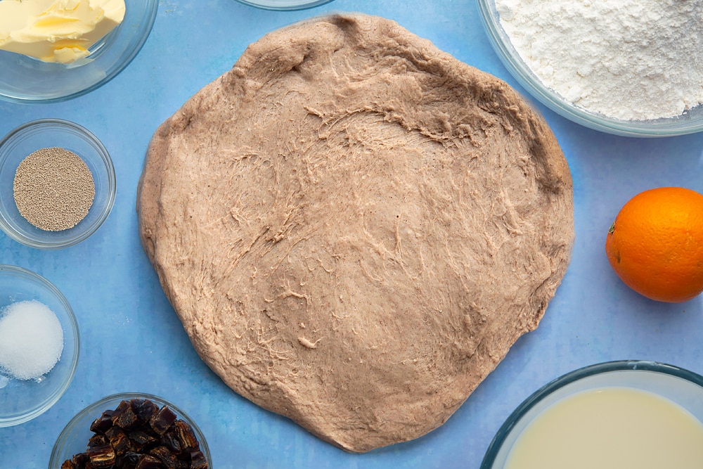 Vegan hot cross buns dough, spread out into a disc. The dough is surrounded by vegan hot cross bun ingredients.